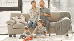 Cheerful family wearing casual clothes sitting in living room while playing and drinking tea during weekend at home in morning